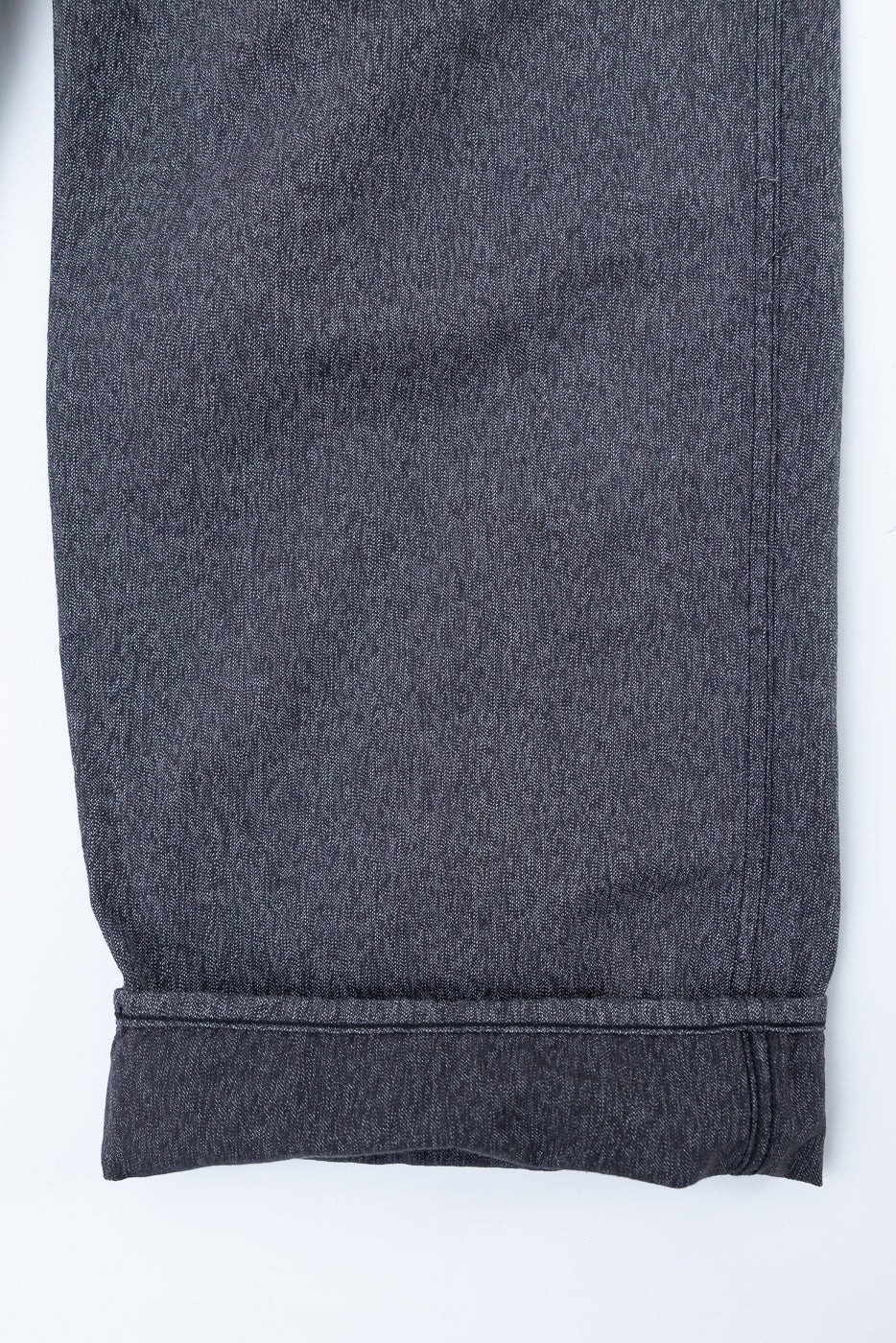 Close-up front view of dark selvedge denim pant leg, showing cuffed hem and fabric texture