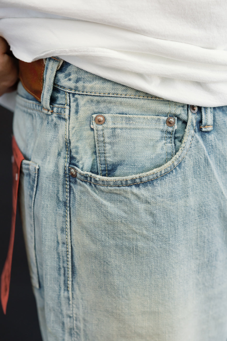 Close-up of male model's back pocket, light-wash denim jeans with copper rivets, athletic build