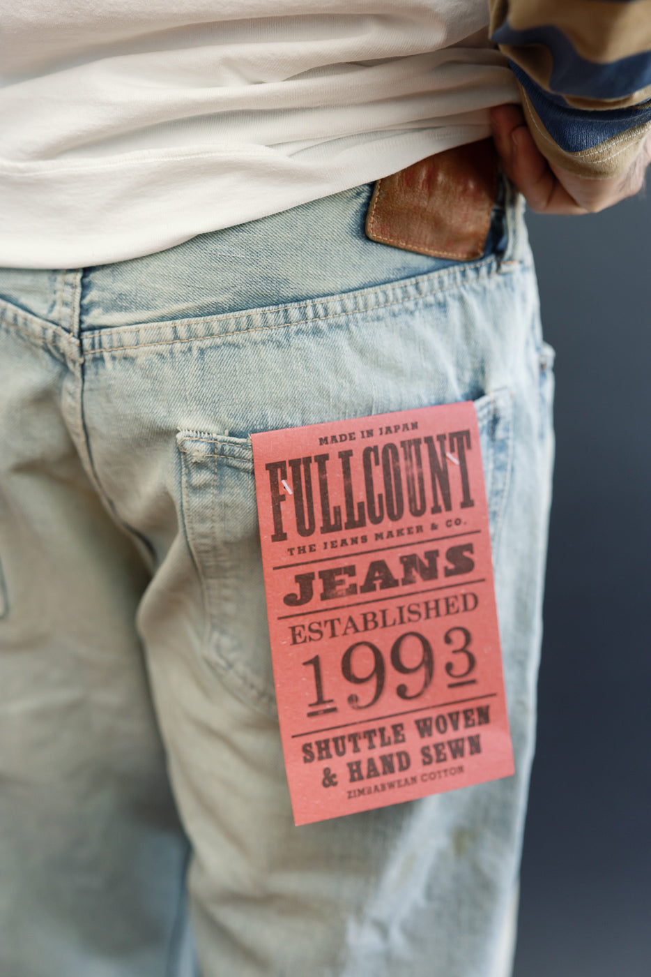 Close-up of male model's back pocket showing Fullcount jeans tag, light wash denim, 5'9