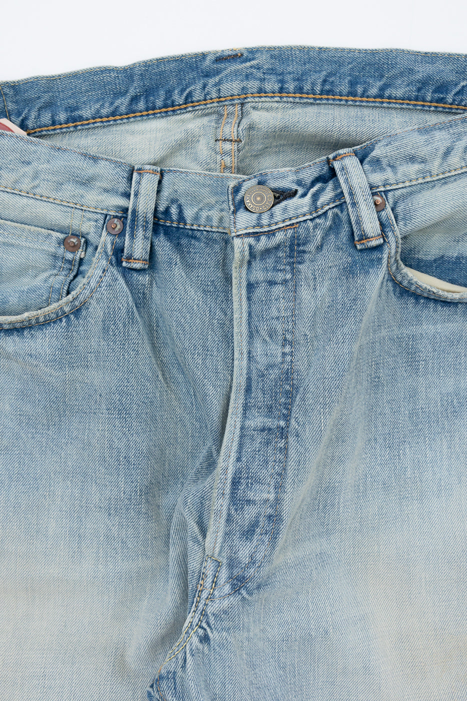 Close-up front view of light wash denim jeans showing button fly, belt loops, and selvedge stitching detail