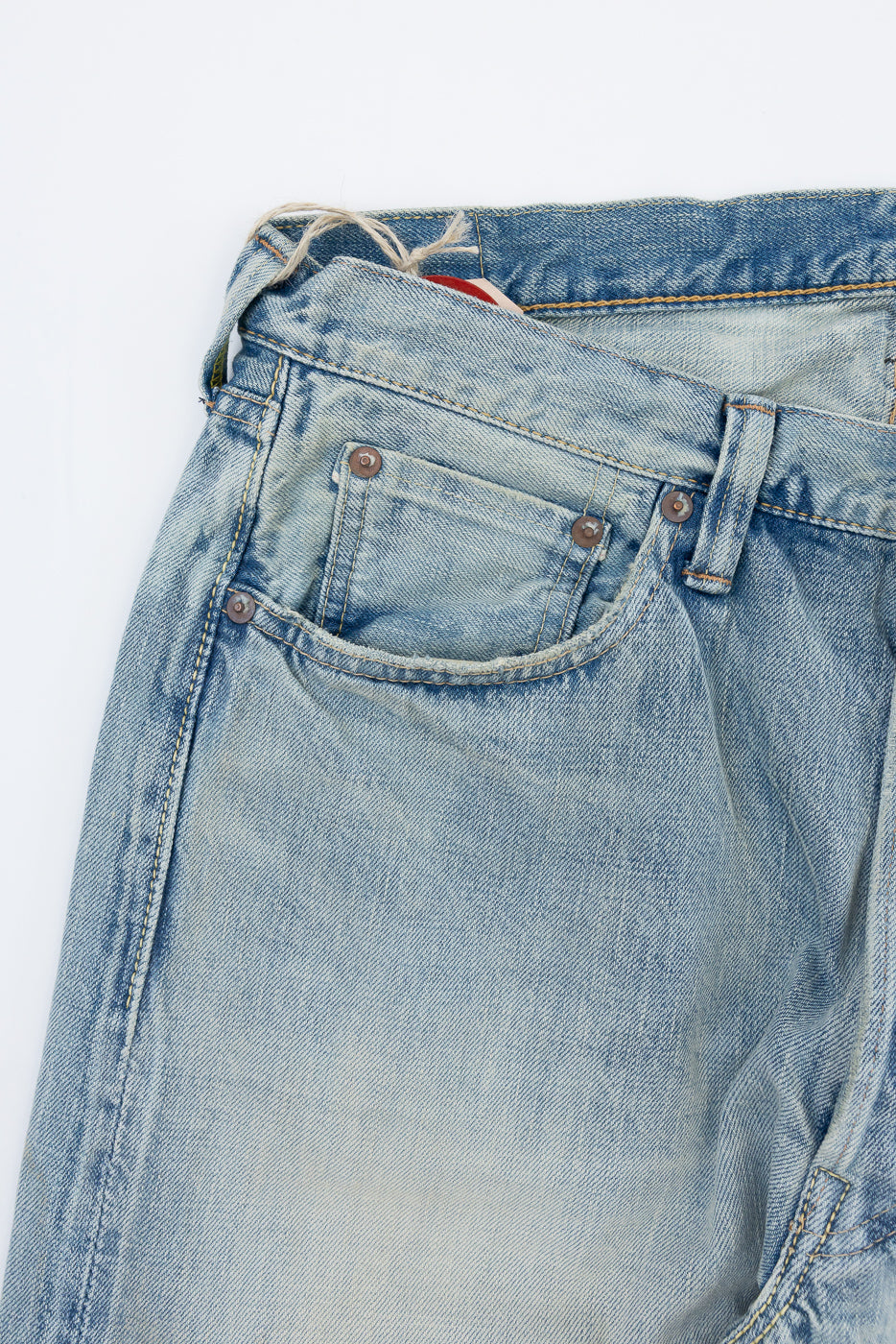 Close-up front view of light wash denim jeans showing button fly, front pocket stitching, and selvedge fabric texture