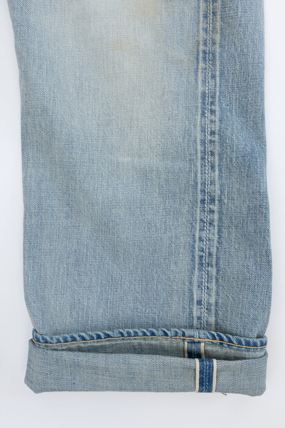 Close-up of light wash selvedge jeans leg, front view, showing raw hem, contrast stitching, and selvedge ID stripe