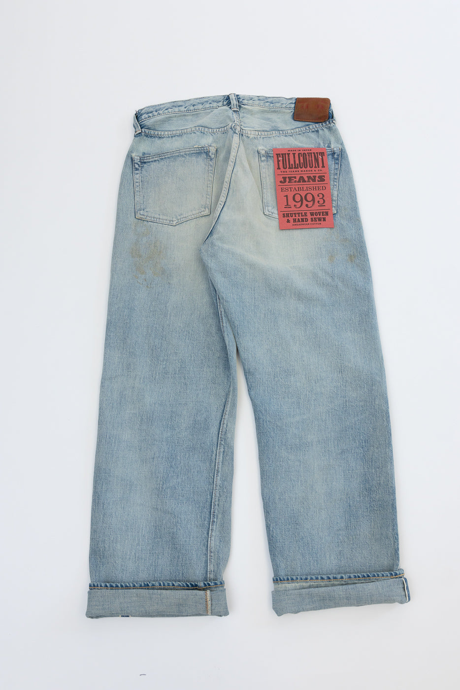 Back view flat lay of light wash selvedge jeans, cuffed hems, red brand patch on right pocket
