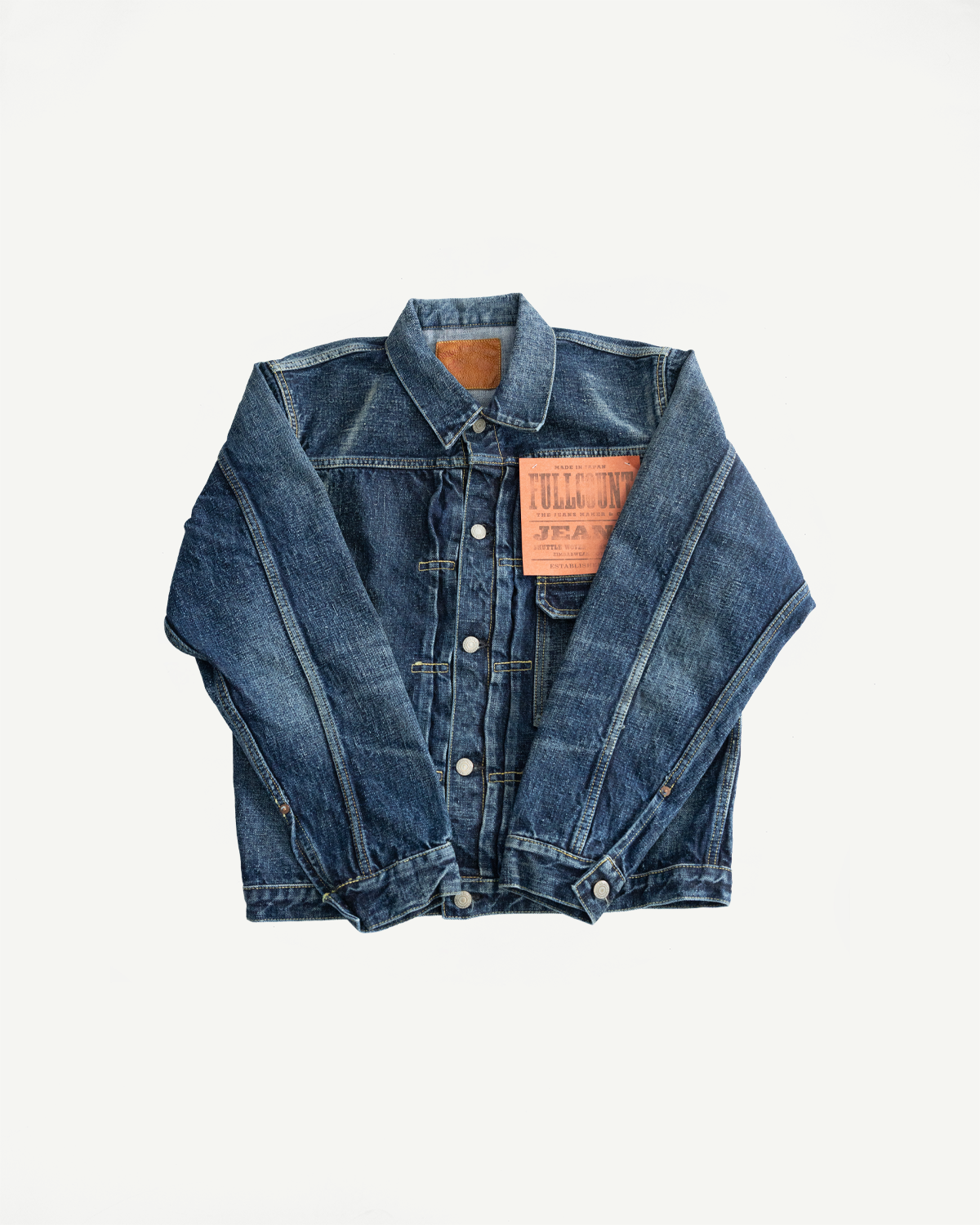 Flat lay front view of hard washed indigo denim jacket with button front, collar, and visible brand patch.