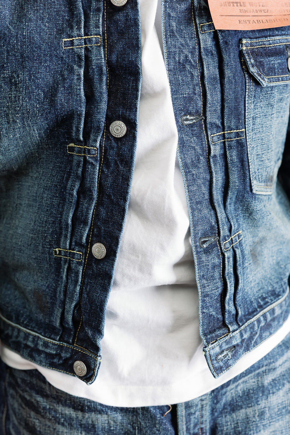 Close-up front view of hard-washed indigo denim jacket, showing button and pocket detail on male model, 5'9