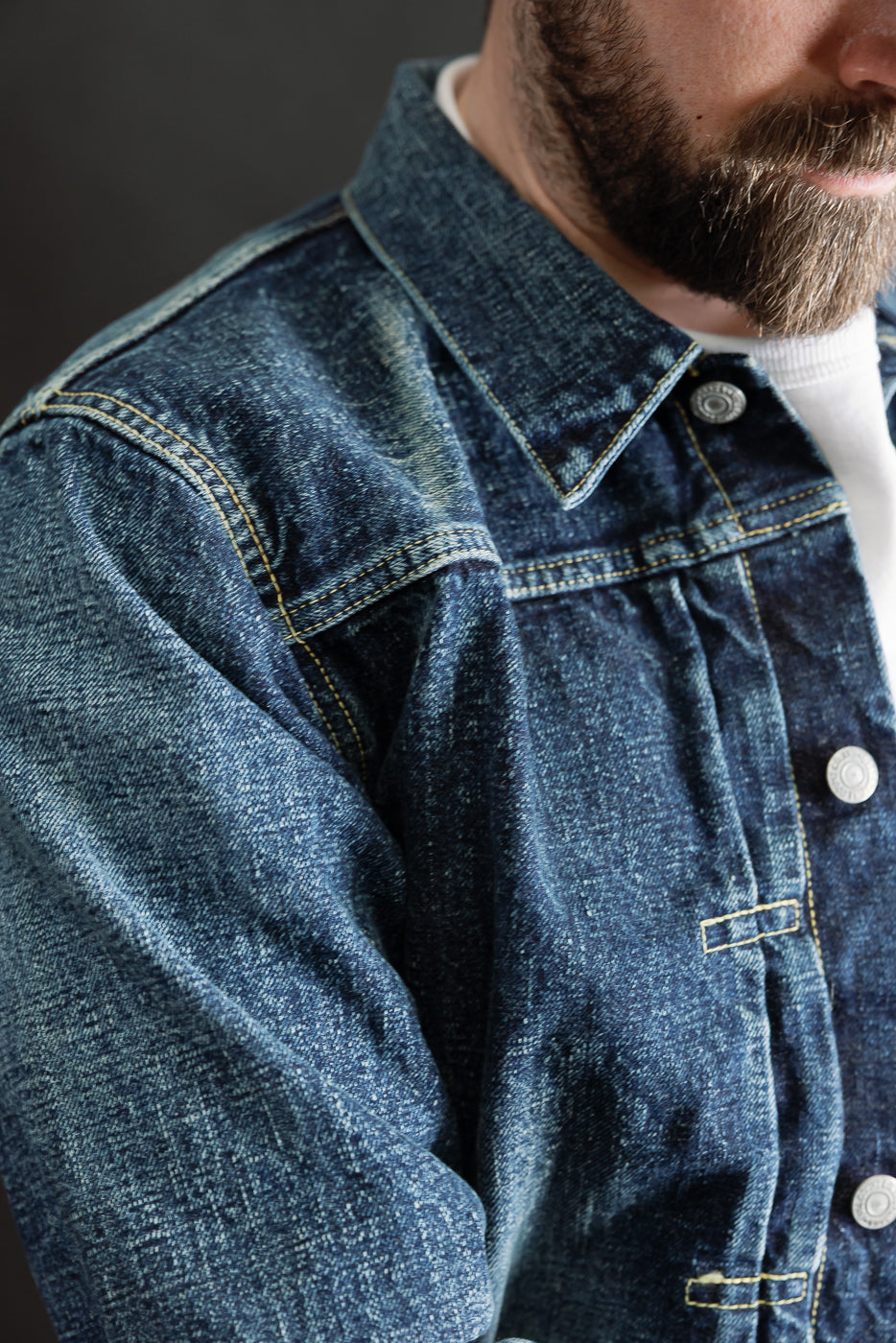 Close-up of front chest and shoulder detail on a hard washed indigo denim jacket; male model, 5'9