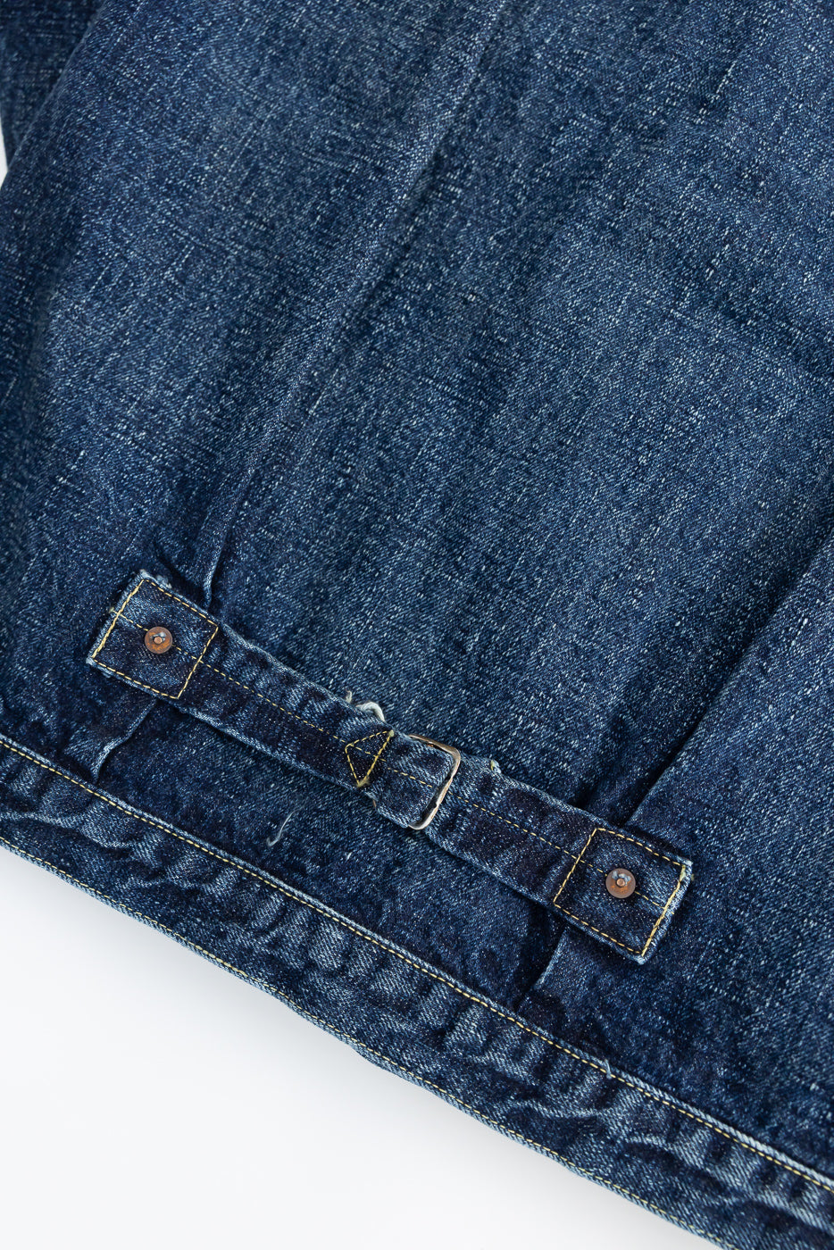Close-up of the back hem and adjustable cinch strap detail on hard washed indigo denim jacket.