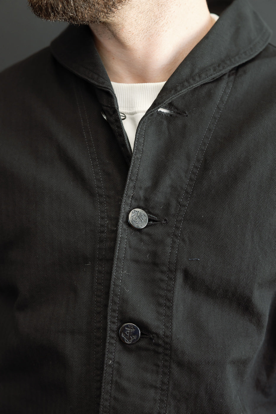 Close-up front view of black herringbone work shirt with anchor buttons, worn by male model, 5'9