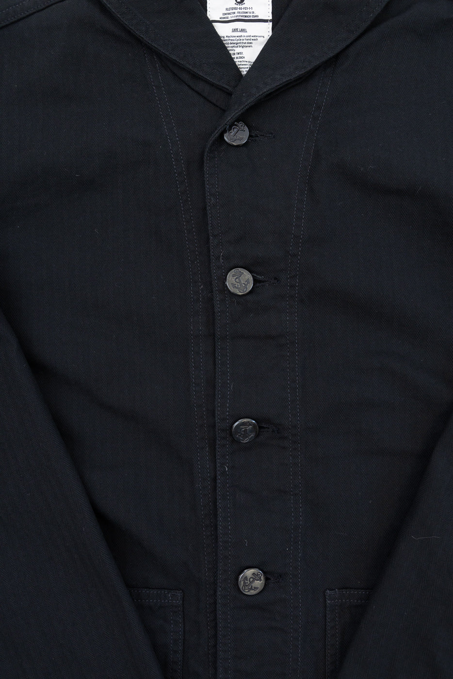 Close-up front view of black shirt with anchor buttons, collar, and care label, showcasing fabric texture.