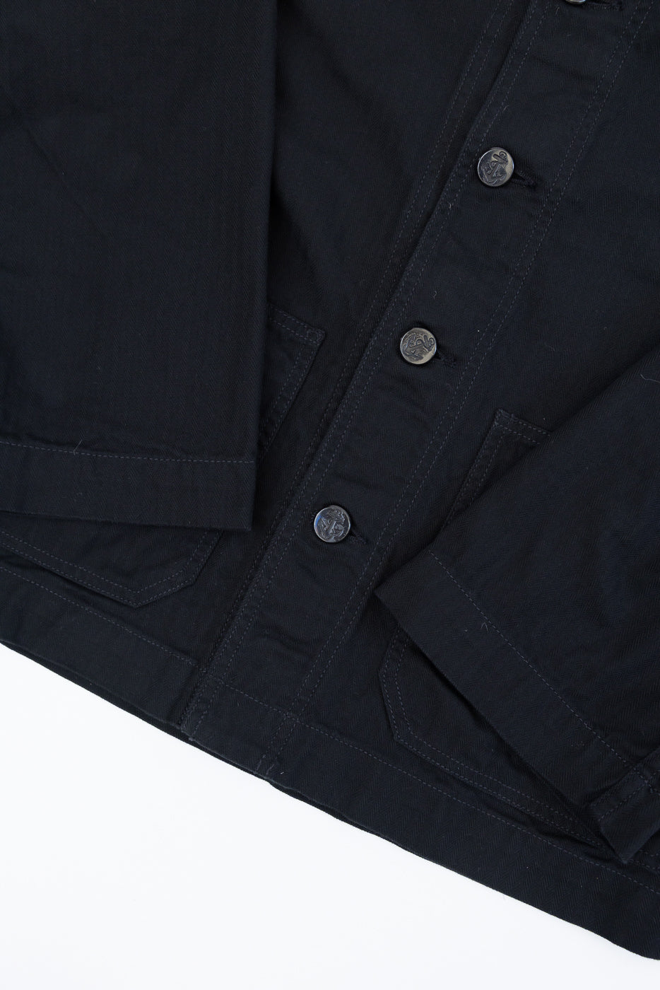 Close-up front view of black jacket with anchor buttons and chest pockets, showcasing fabric texture and stitching details.