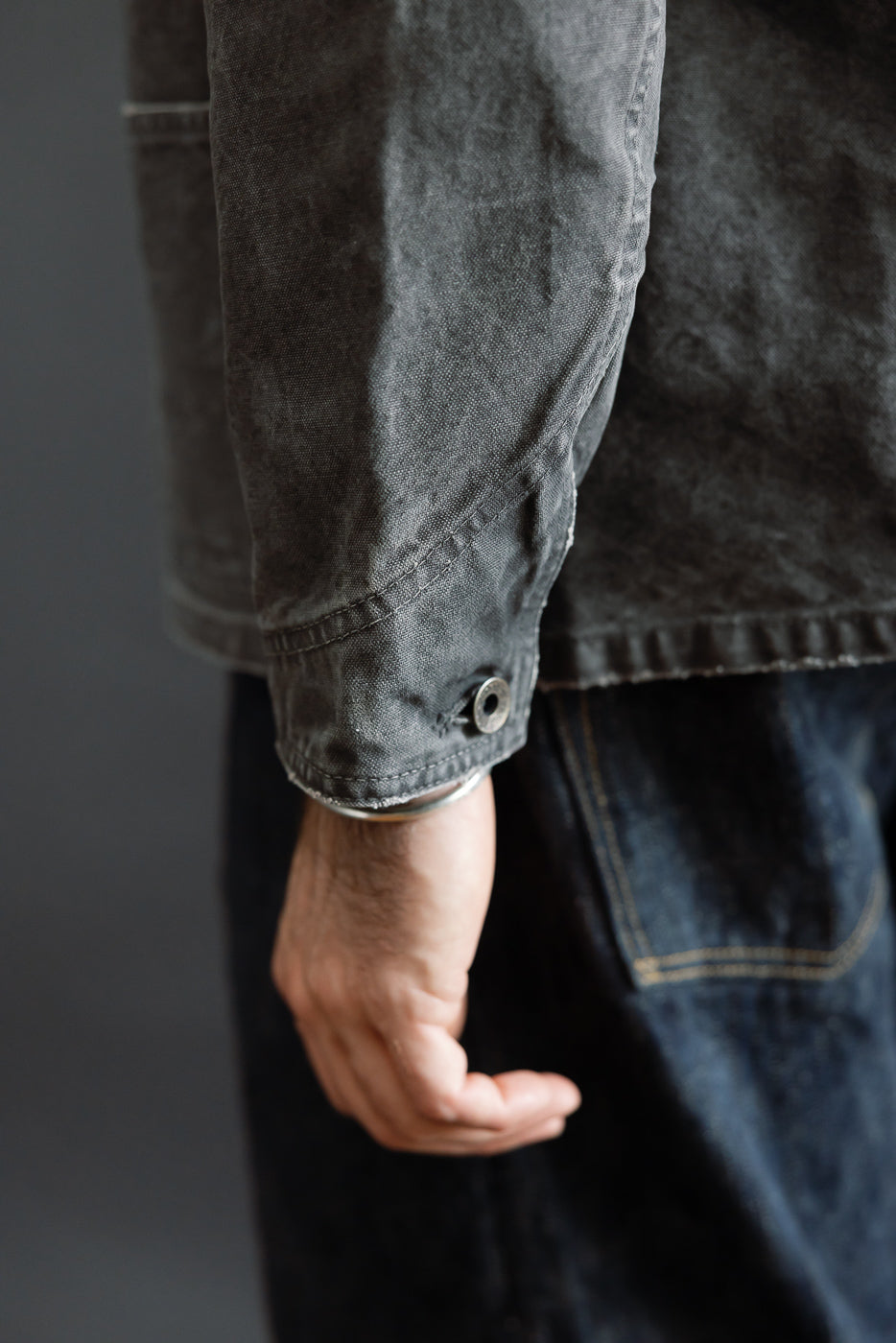 Close-up of male model's arm showing dark denim jacket sleeve with button cuff detail
