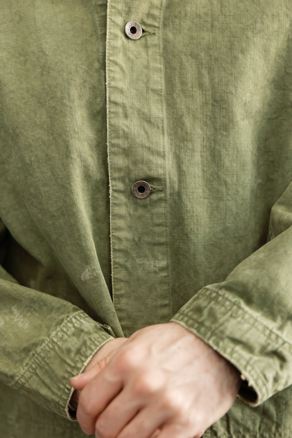 Close-up front view of olive green shirt with metal buttons, worn by male model, 5'9