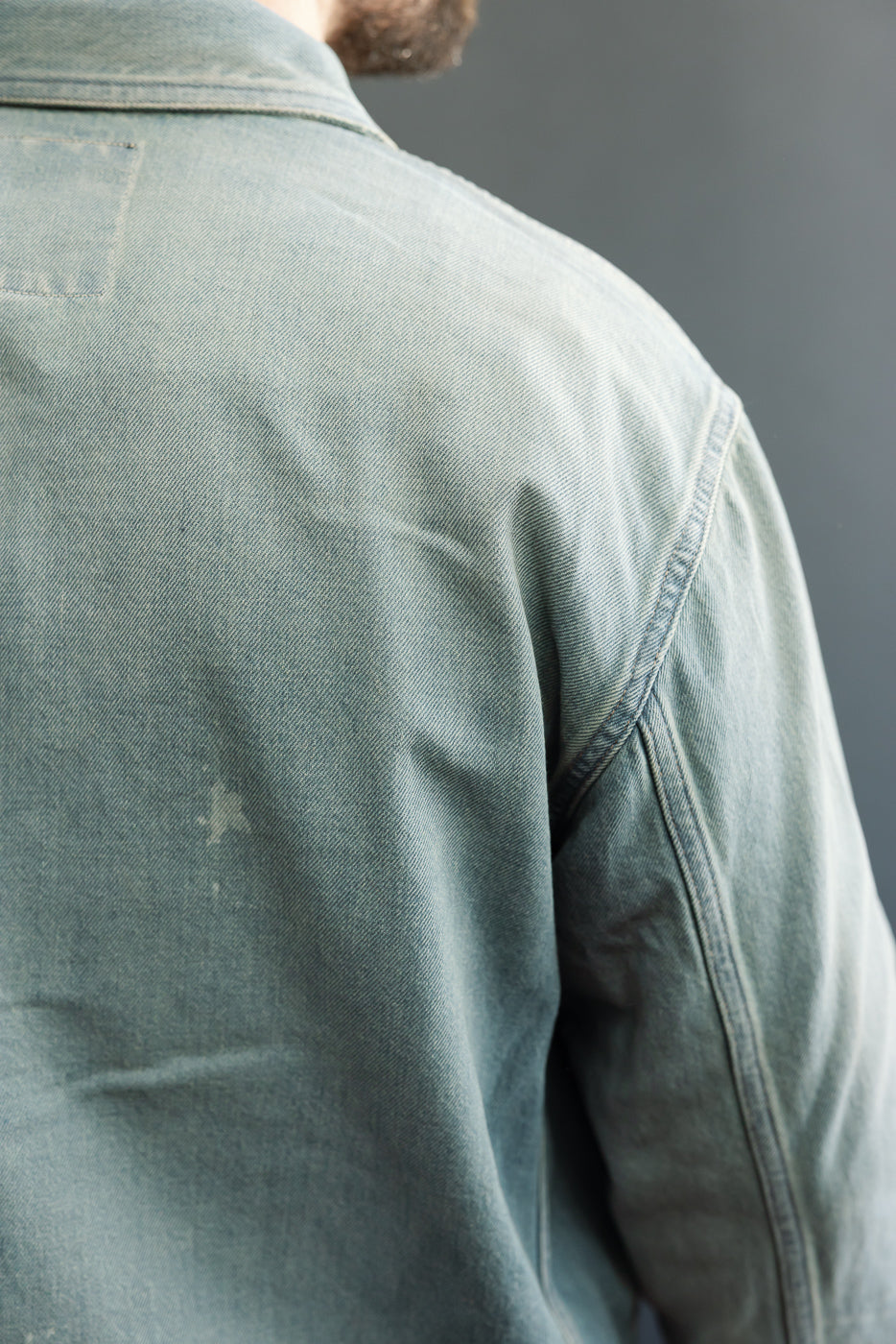 Back view of male model in faded denim shirt, showing shoulder seam and fabric texture