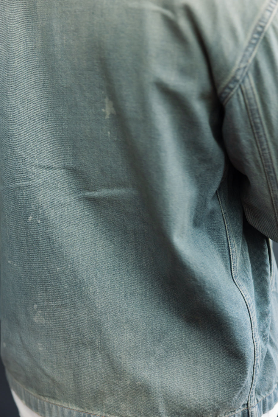 Close-up of back side of denim jacket, showcasing fabric texture and stitching details.