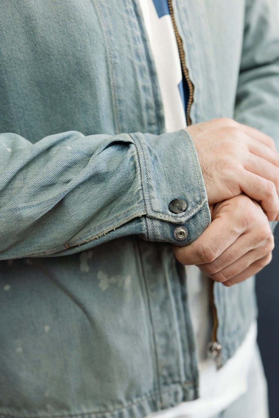 Close-up of male model's arm in light denim jacket, showcasing buttoned cuff and fabric texture.
