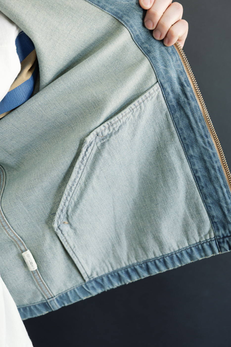 Close-up of male model's denim jacket front, showing pocket, zipper, and tag details