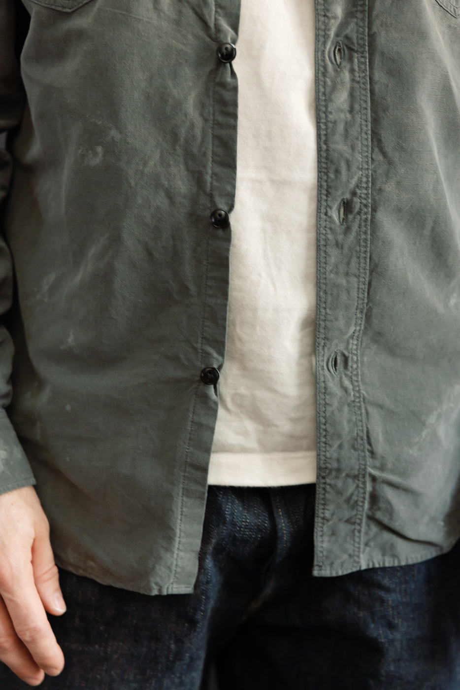 Close-up front view of olive shirt with black buttons, worn by male model, 5'9