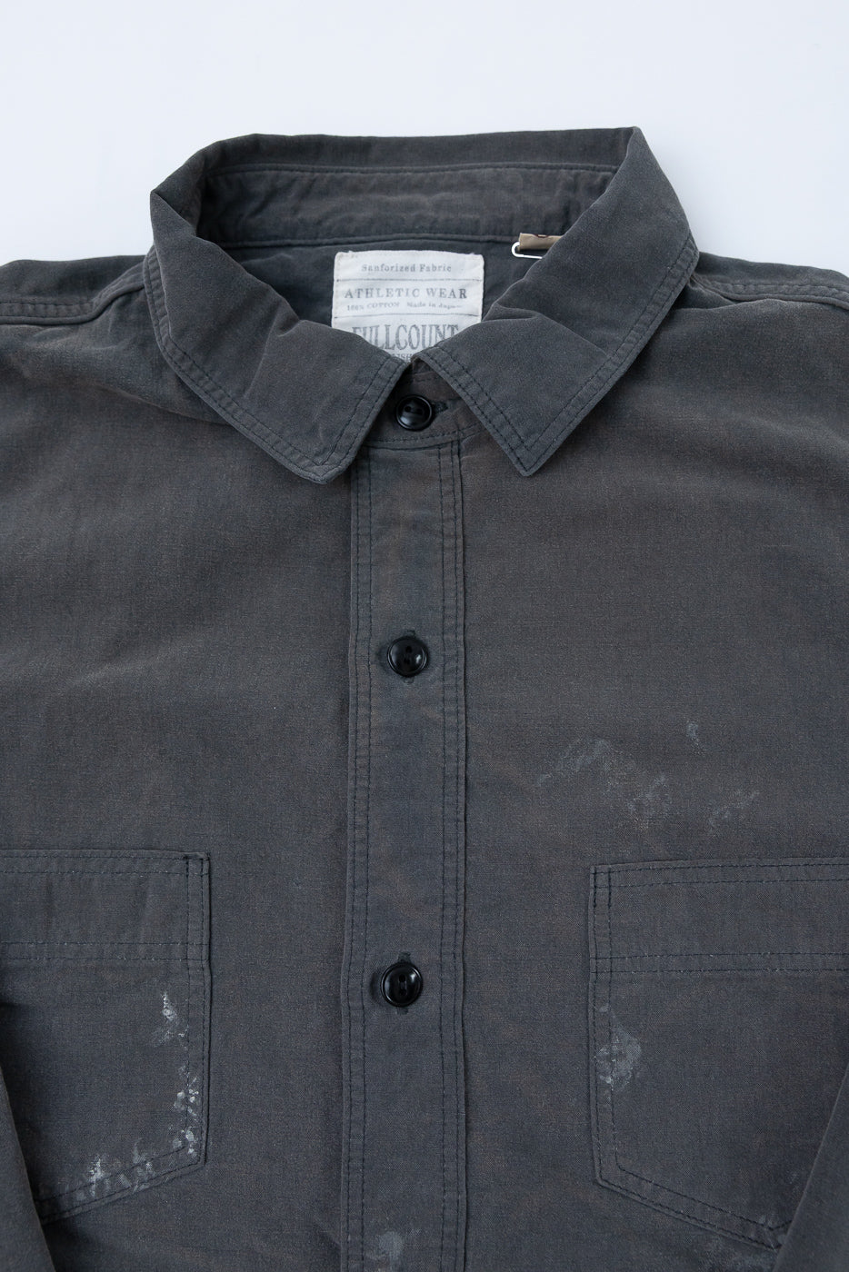 Close-up front view of dark gray work shirt: button-down collar, black buttons, chest pockets, sanforized fabric tag