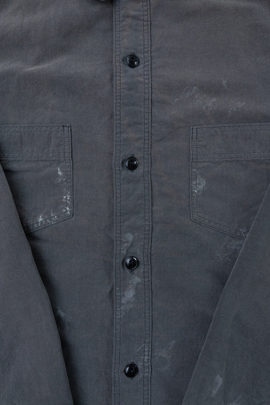 Close-up front view of dark gray shirt with black buttons and chest pockets, showing fabric texture.