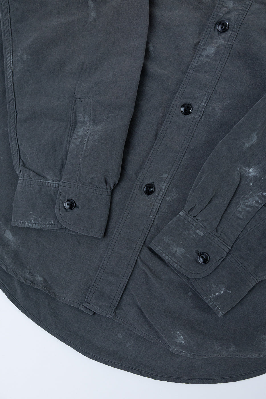 Close-up front view of dark gray washed shirt with black buttons, chest pockets, and curved hem detail.