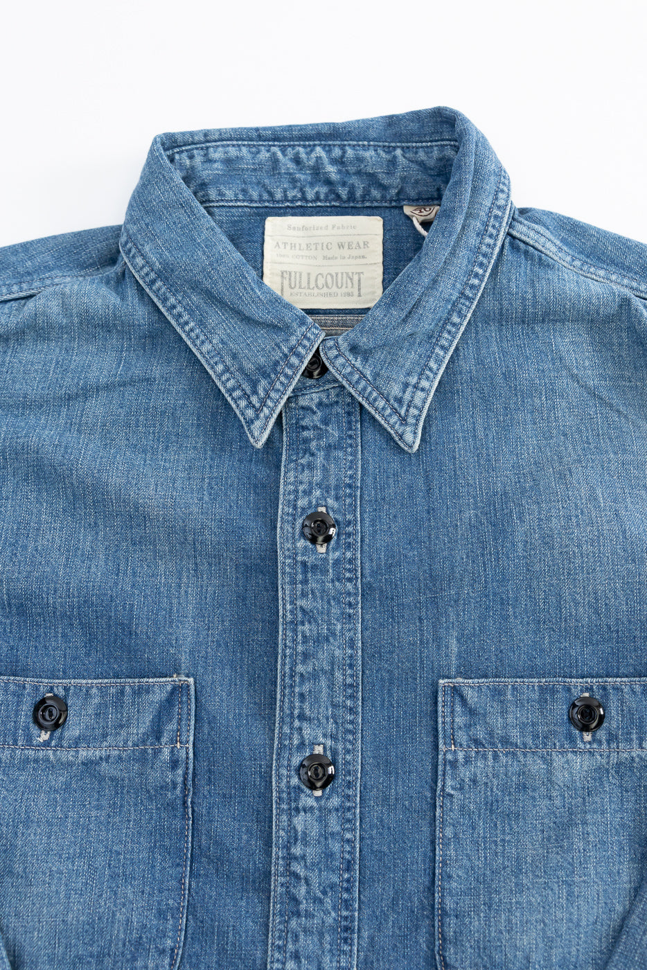 Close-up front view of indigo denim work shirt showing collar, tag, buttons, and chest pockets.