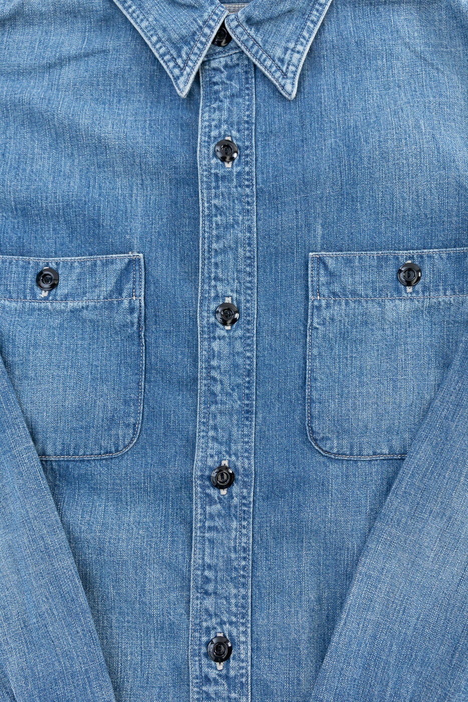 Close-up front view of denim work shirt, showing button-down placket, two chest pockets, and pointed collar.
