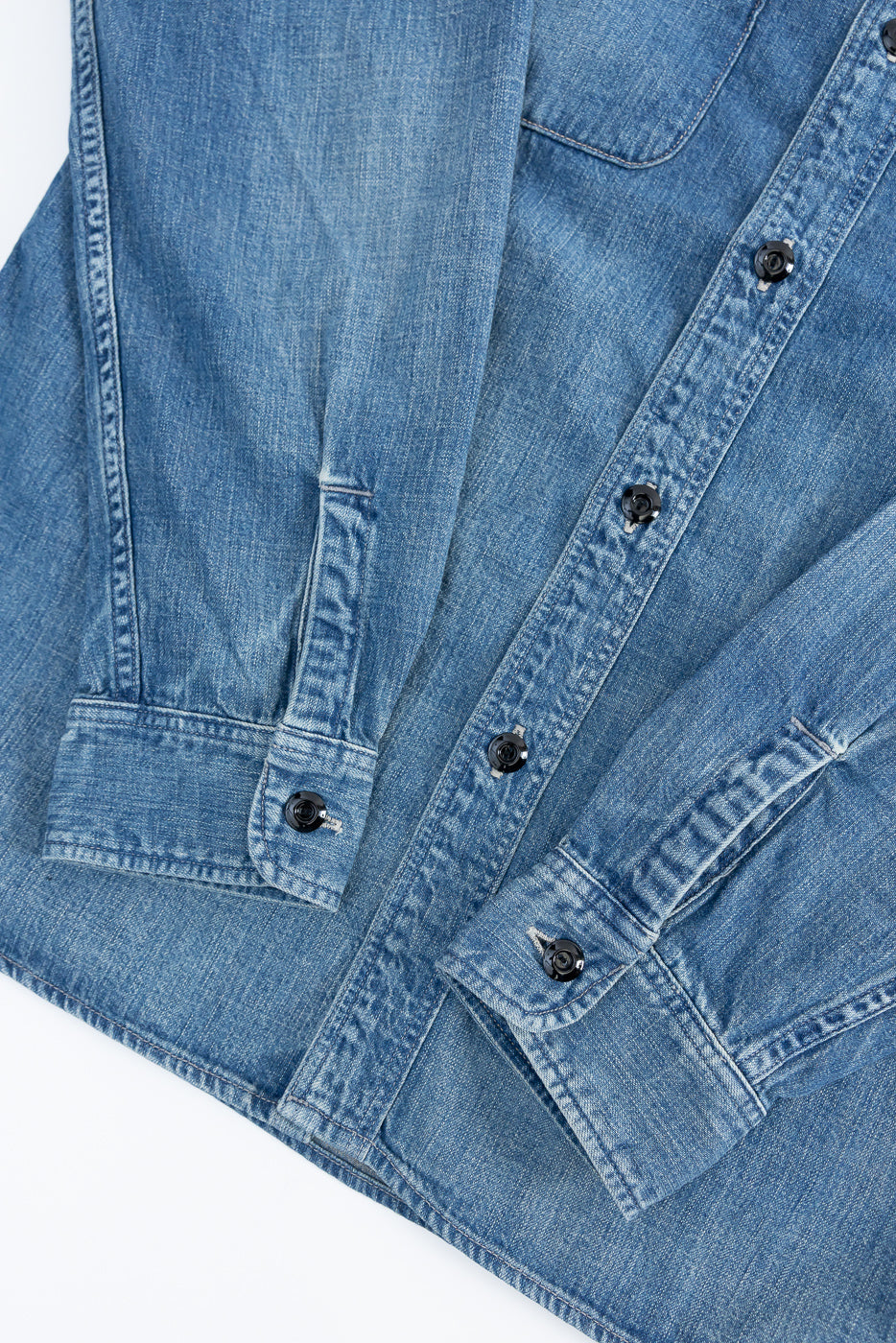 Close-up of front denim work shirt, showing button cuffs, sleeve detail, and indigo texture.