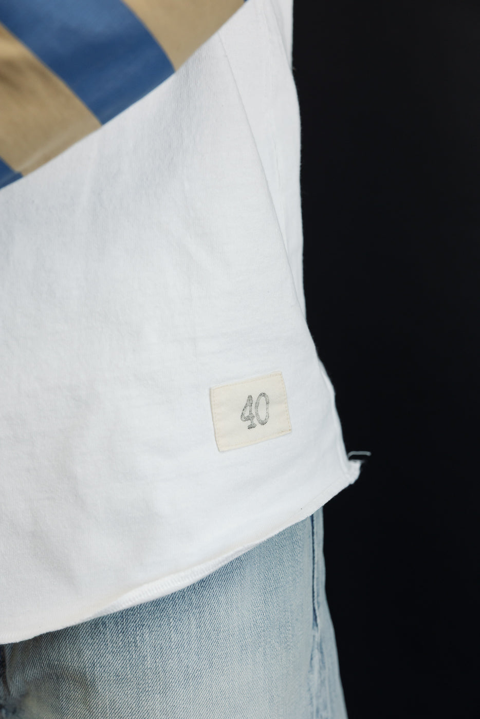 Close-up side view of white tee with '40' tag, worn by male model, athletic build, paired with light denim