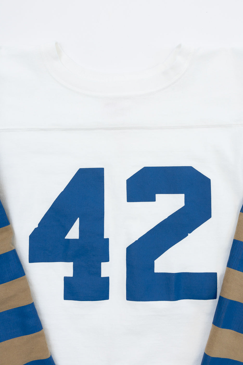 Close-up front view of white long-sleeve jersey with bold blue '42' number, striped blue and tan sleeves, ribbed crew neck.