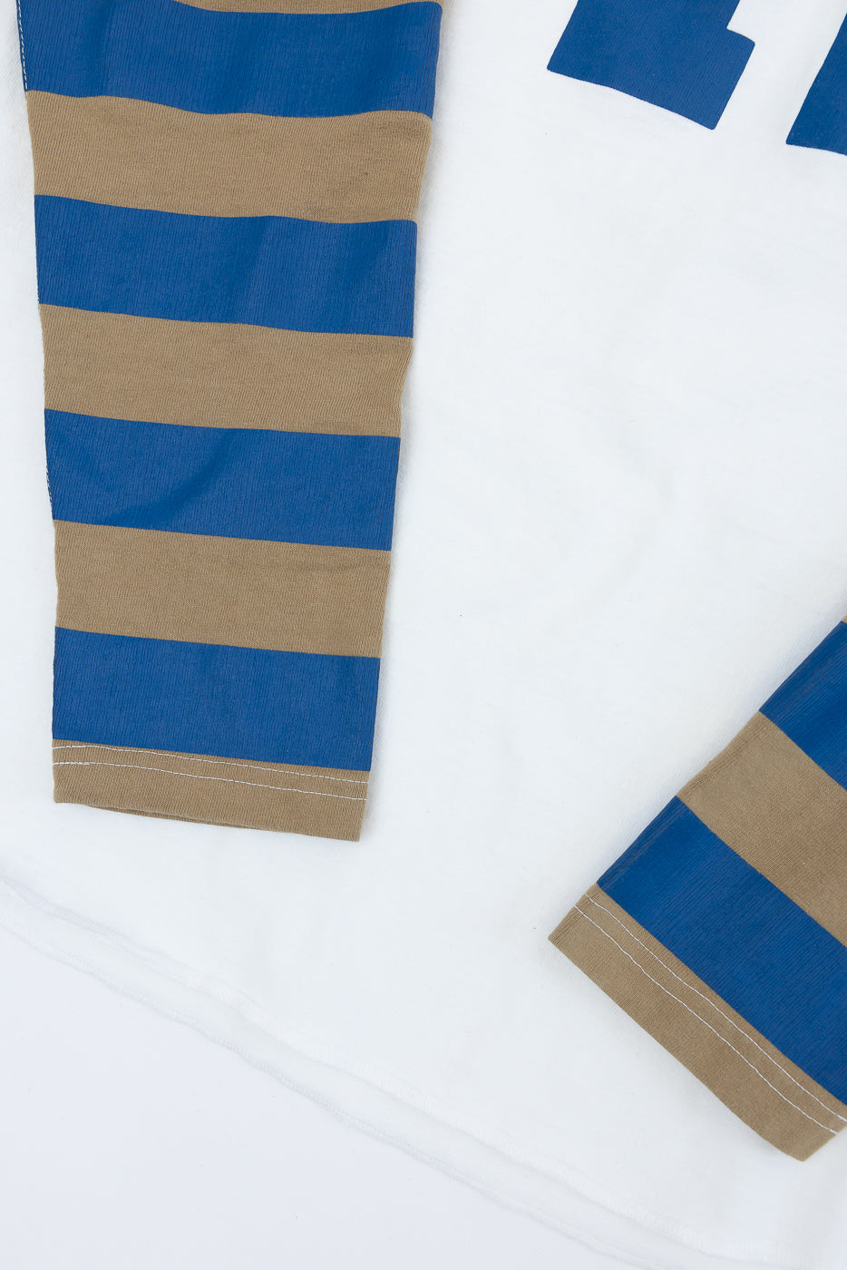 Close-up of striped long sleeve shirt sleeves, front view, blue and tan horizontal stripes, ribbed fabric, white contrast stitching at cuffs