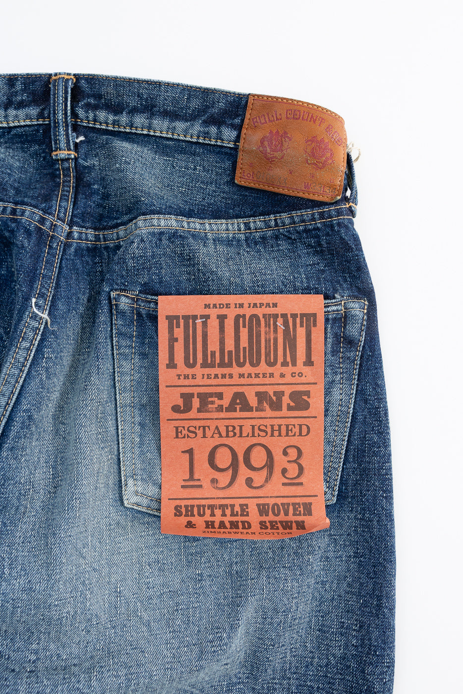 Close-up of back side of hard washed indigo denim jeans, showing leather patch, rear pocket, and product tag details.