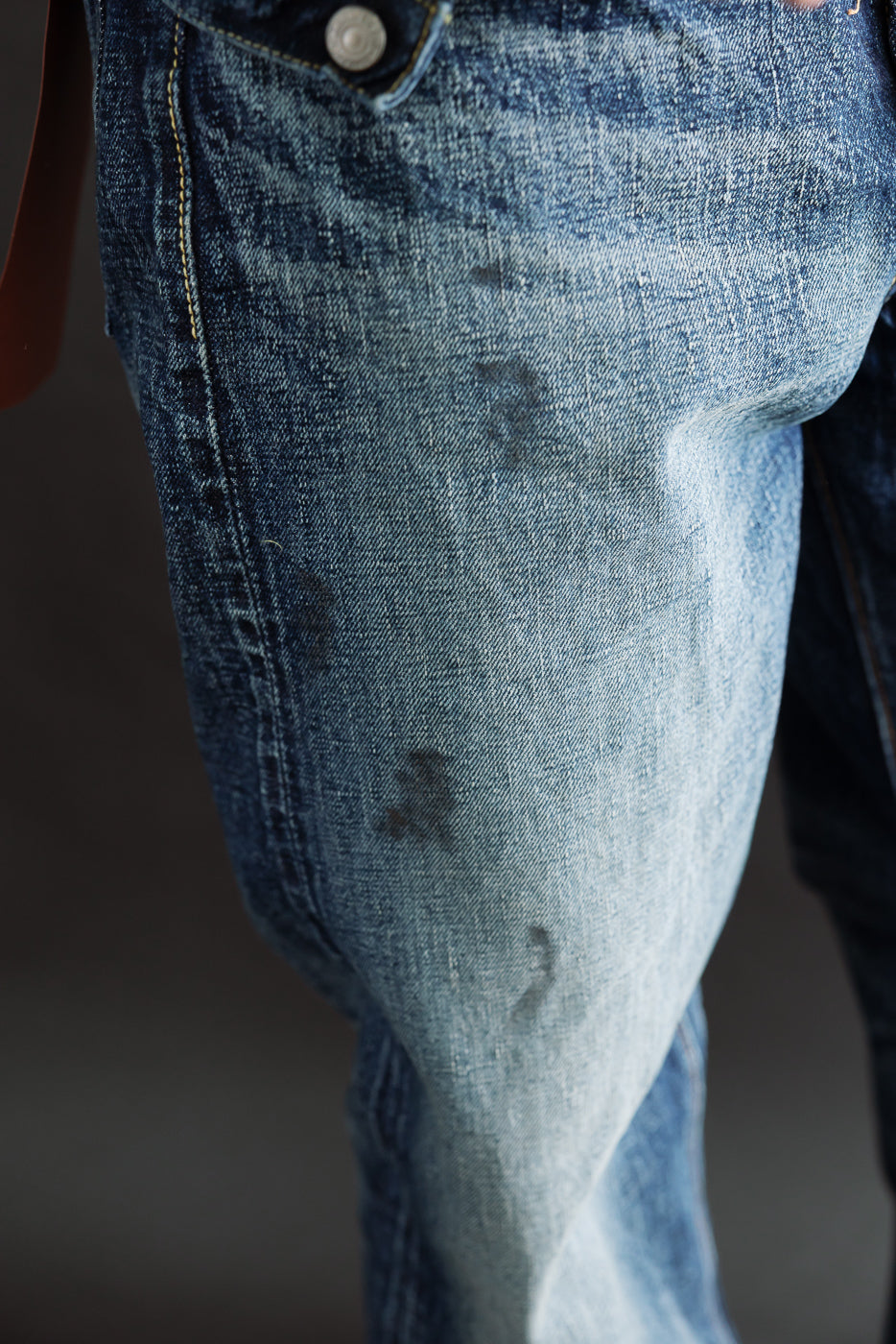 Close-up of front left thigh on hard-washed indigo denim, showing textured fade details. Male model, 5'9