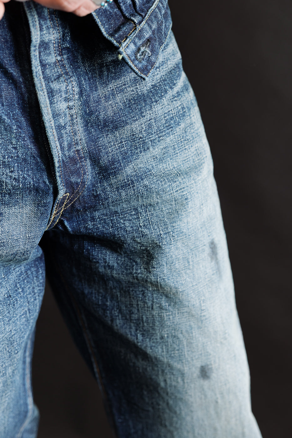 Close-up of front upper thigh and fly on hard washed indigo wide denim, showing fabric texture.