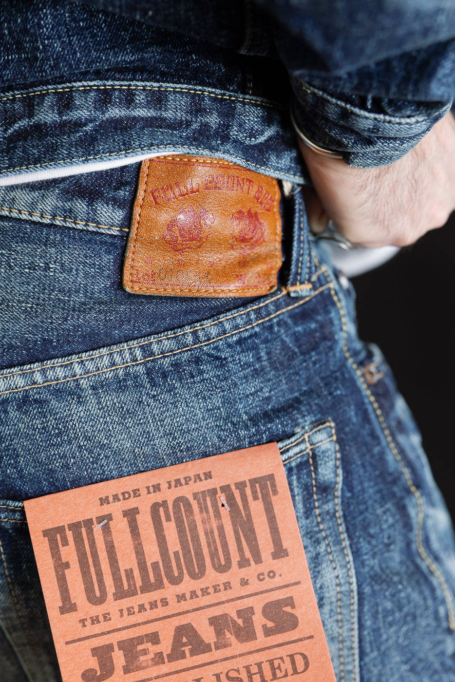 Close-up of back waist and pocket of men's hard washed indigo denim jeans, rear view, leather patch and product tag visible, on 5'9
