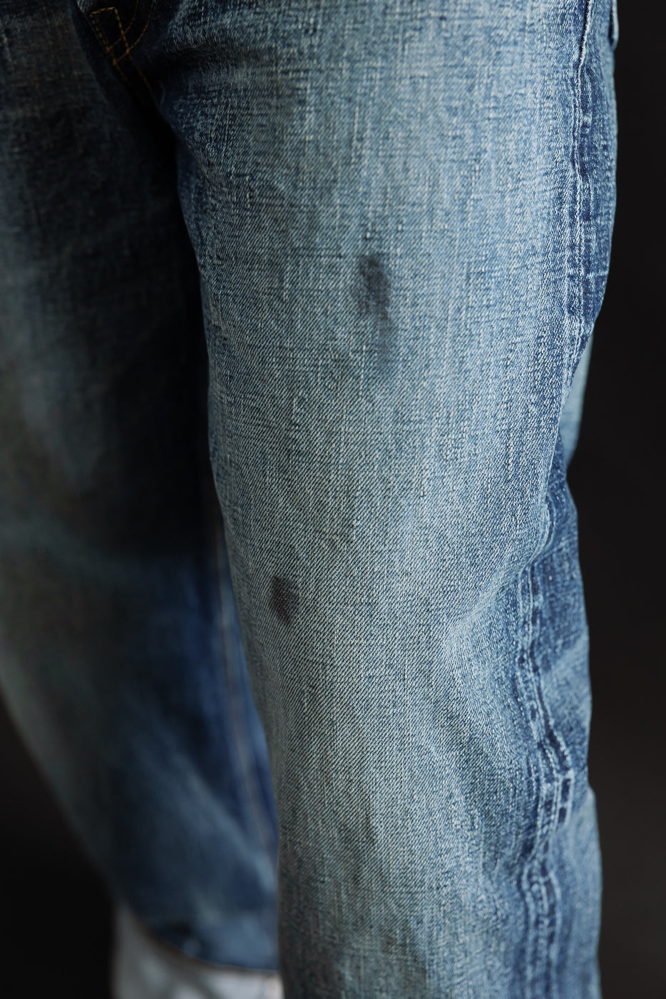 Close-up of male model’s front thigh, showing hard-washed indigo denim fabric texture.