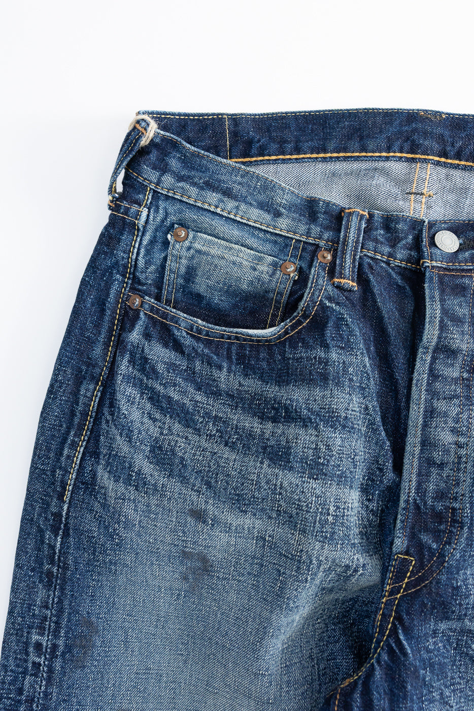Close-up of denim jeans front side, showing pocket rivets and hard-washed indigo fabric texture
