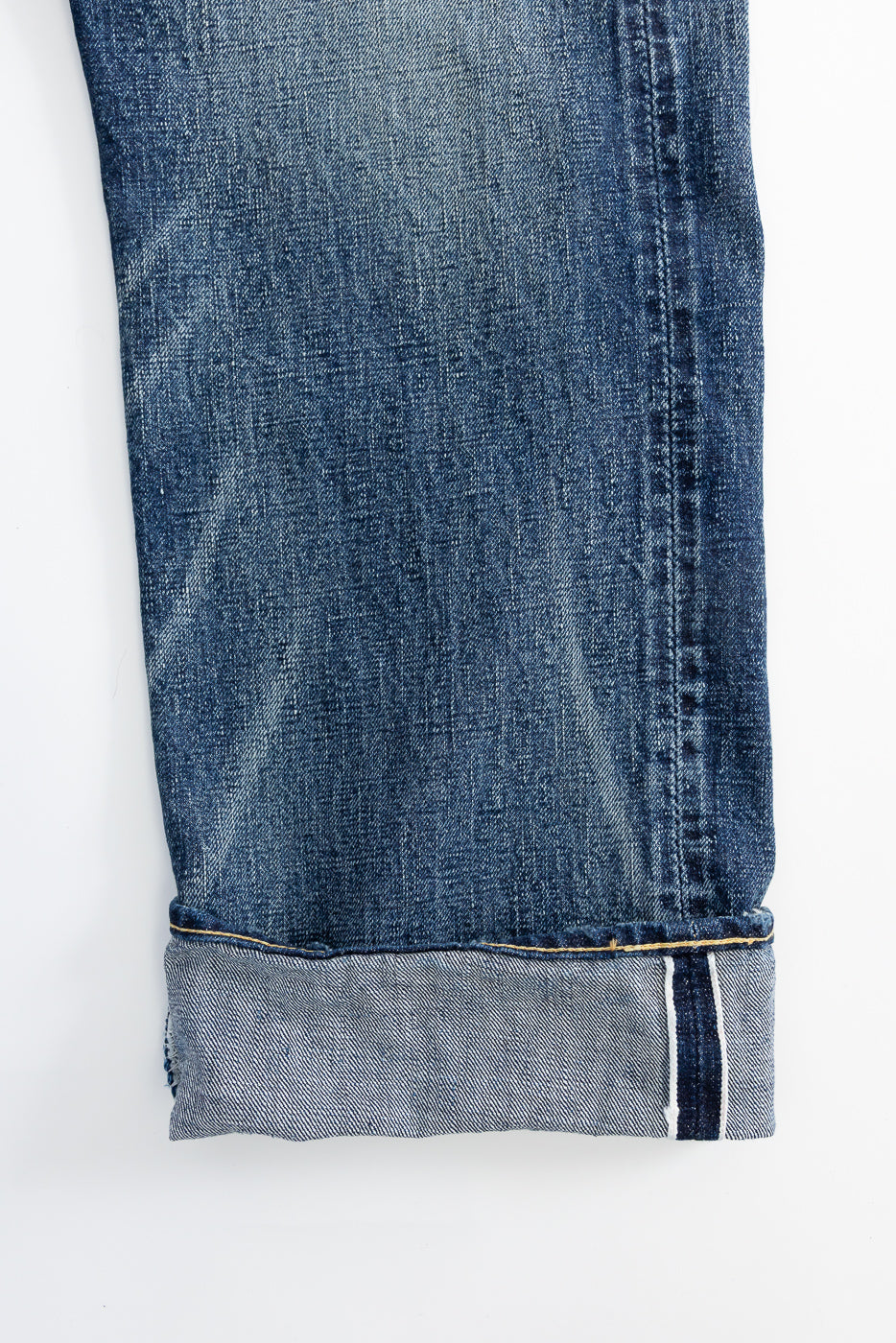 Close-up of front left leg hem on hard-washed indigo selvedge denim jeans, showing cuff detail and fabric texture.