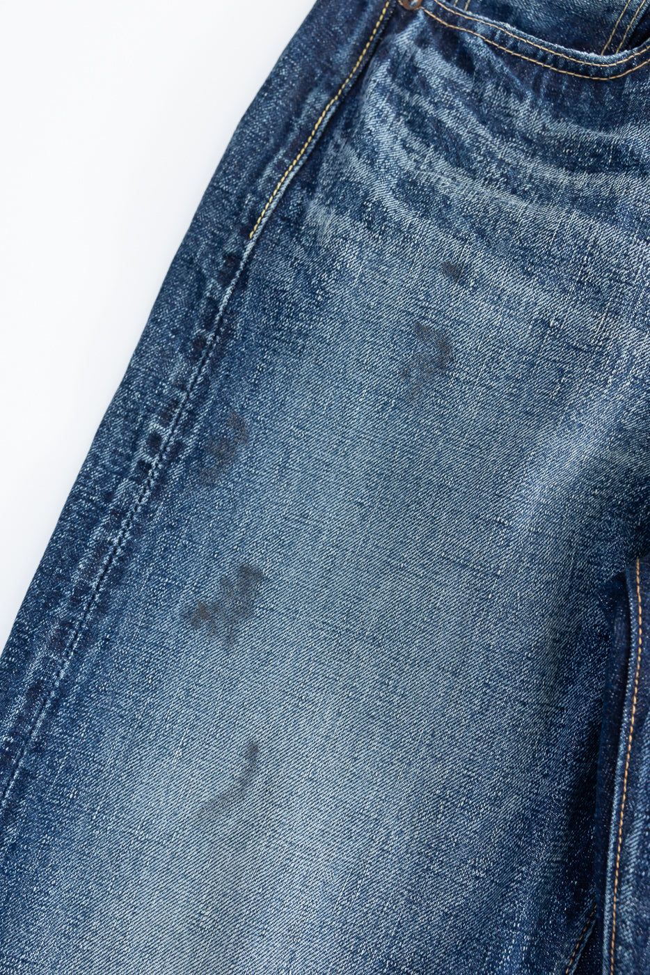 Close-up of front left leg of hard-washed indigo denim, showing fabric texture and fade details.