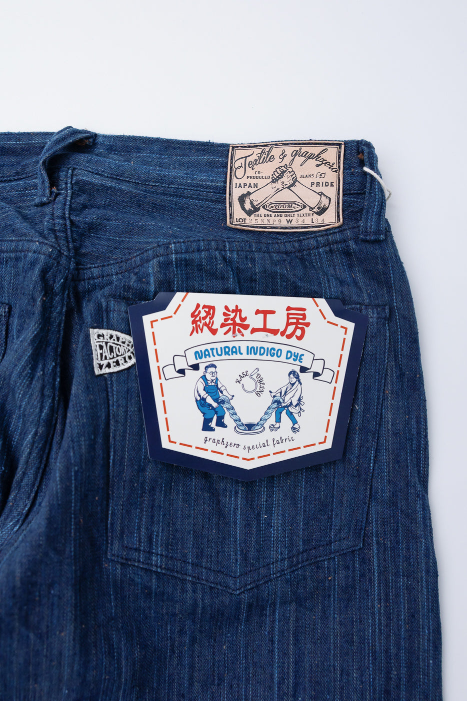 Close-up of back right side of Graph Zero 13oz indigo selvedge jeans, showing leather patch, fabric texture, and paper tag details.