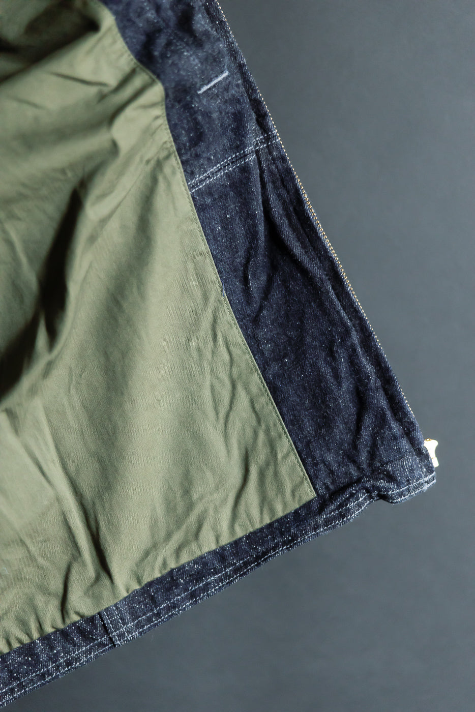 Close-up of jacket's interior: olive lining, raw denim exterior, zipper detail, and contrast stitching