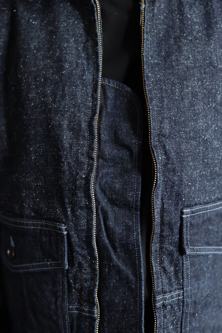 Close-up front view of dark denim jacket showing zipper, pockets, and fabric texture