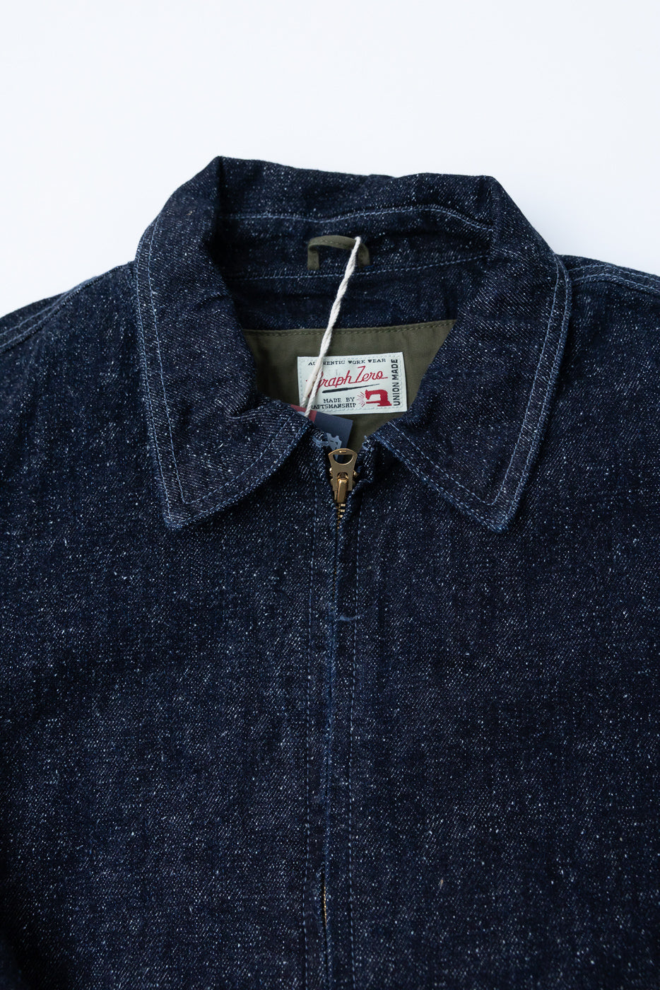 Close-up front view of dark selvedge denim jacket with collar, zipper, and Graph Zero tag detail