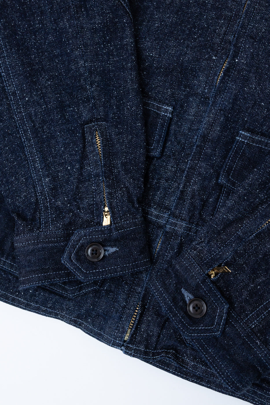 Close-up front view of dark selvedge denim jacket showing button closures, gold zippers, and stitch details