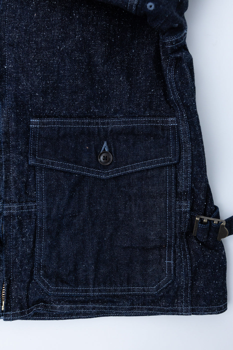 Close-up front view of dark selvedge denim jacket showing chest pocket, button, and stitch details
