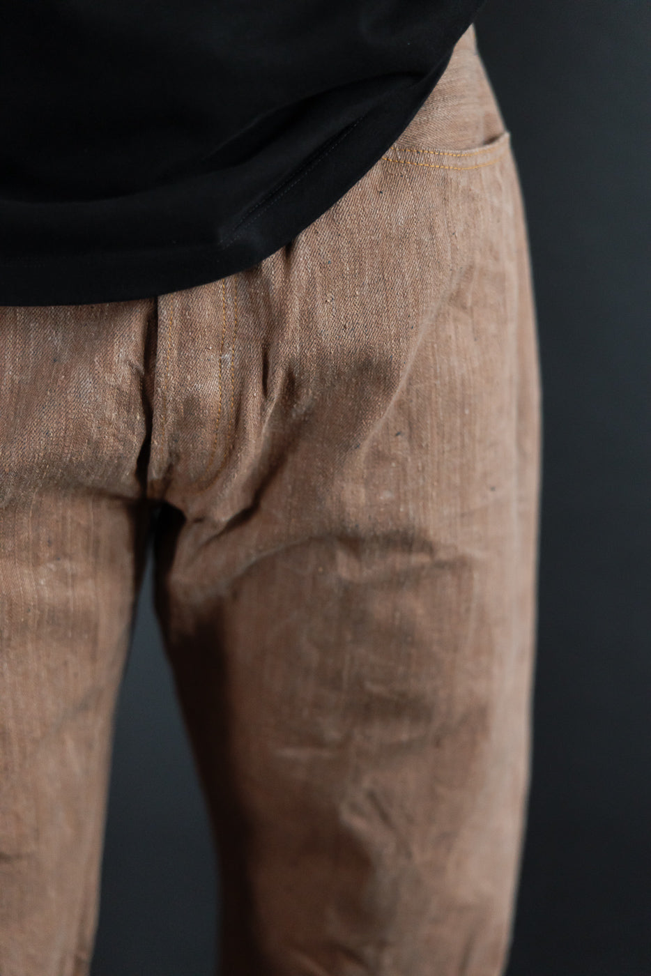 Close-up front view of male model's brown selvedge pants, showing texture, stitching, and pocket detail
