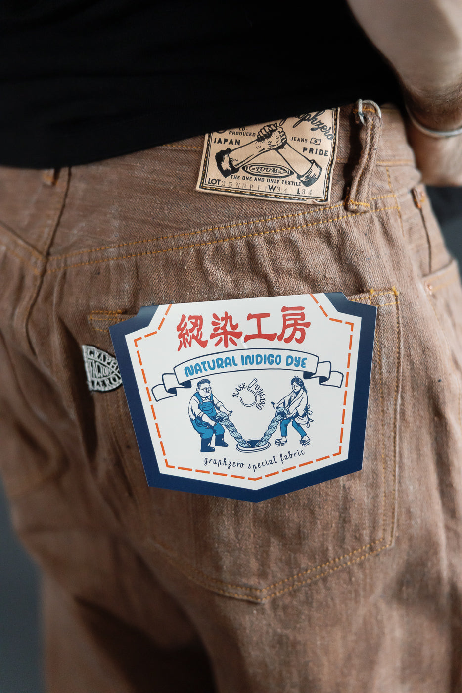 Close-up back view of men's selvedge jeans showing natural indigo dye tag, fabric texture, and waist label on athletic build model