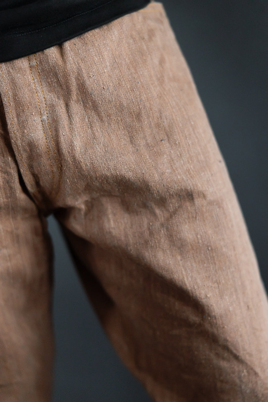 Close-up side view of men's selvedge pants, showcasing fabric texture and stitching detail on athletic build model.