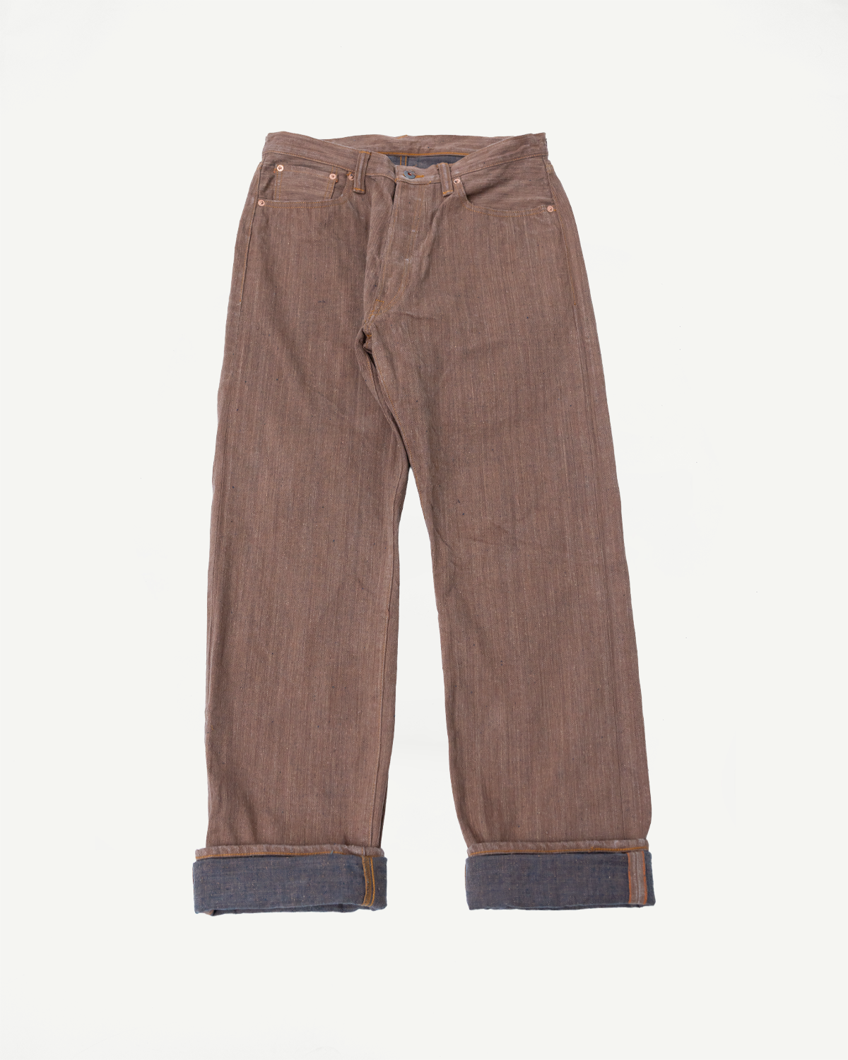 Flat lay front view of brown selvedge denim jeans with cuffed hems showing indigo interior, copper rivets, and button fly.