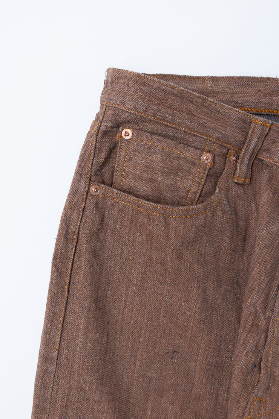 Close-up front view of selvedge denim jeans showing copper rivets, orange stitching, and textured fabric weave