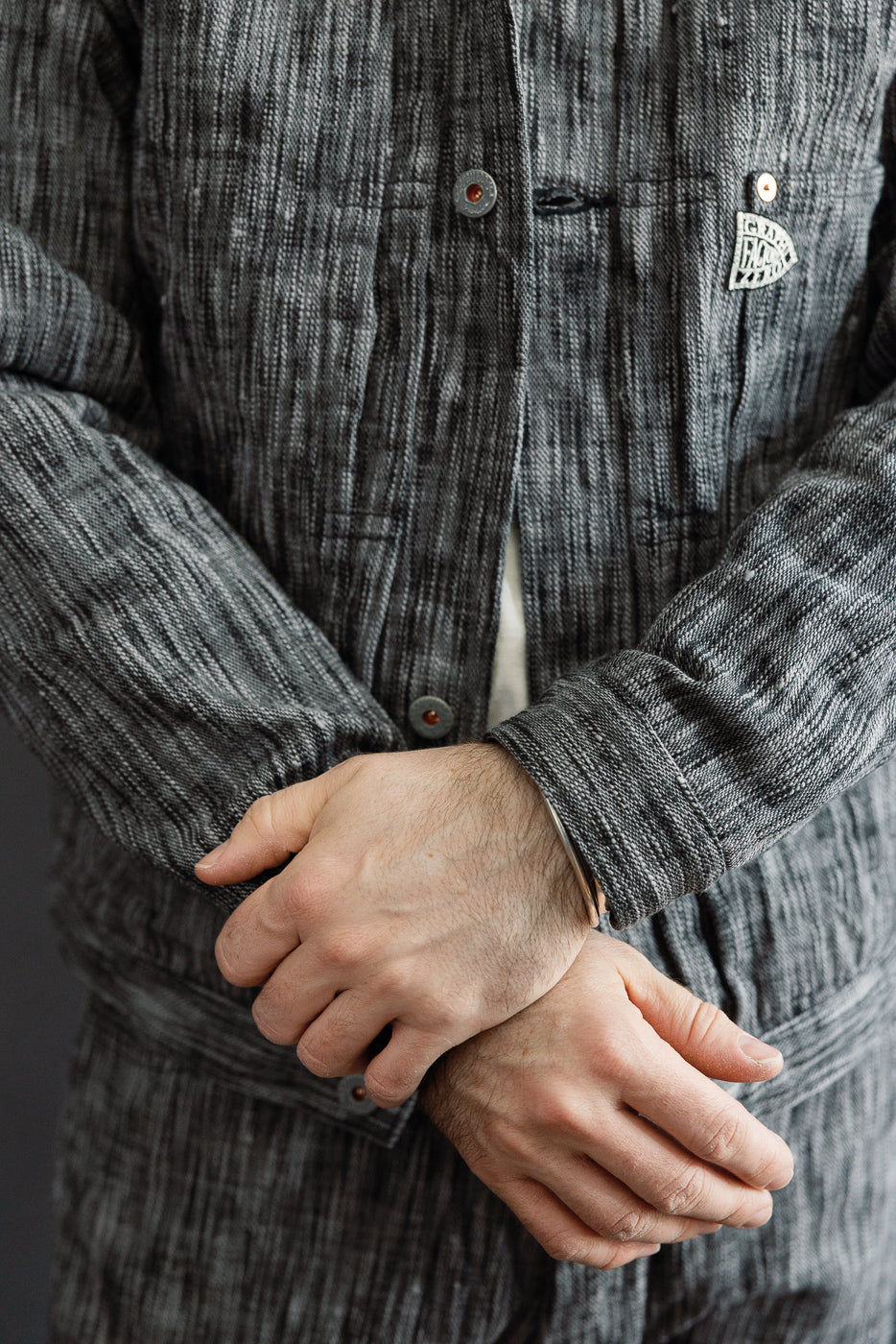 Close-up front view of male model wearing textured gray button-up shirt with chest pocket, metal buttons, and woven label.